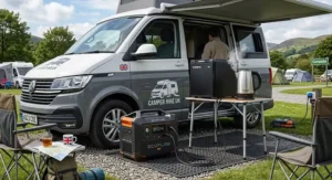 A heavy-duty portable power station powering a mini fridge and an electric kettle outside a campervan at a British campsite.